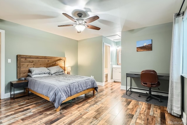 bedroom with light wood-type flooring, baseboards, ensuite bathroom, ceiling fan, and a desk