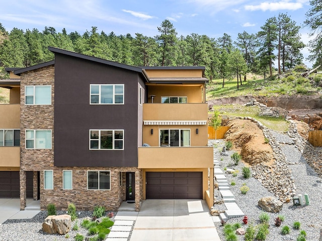 766 Dreamcatcher Ln, Evergreen, CO 80439 - view of front facade featuring stucco siding, concrete driveway, a garage, stone siding, and a balcony