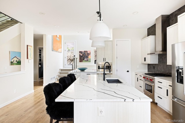 766 Dreamcatcher Ln, Evergreen, CO 80439 - kitchen with appliances with stainless steel finishes, wall chimney range hood, white cabinets, a center island with sink, and light wood finished floors