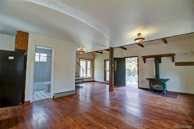 unfurnished living room with dark hardwood / wood-style flooring, a wood stove, and a baseboard radiator