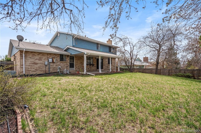 rear view of house featuring a patio, a chimney, brick siding, fence, and a lawn
