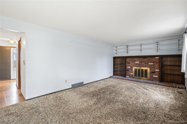 unfurnished living room with visible vents, baseboards, a brick fireplace, a textured ceiling, and carpet floors