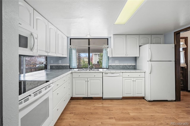 kitchen with white cabinets, a sink, light wood-type flooring, white appliances, and tile counters