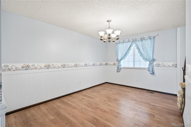 empty room with a wainscoted wall, a notable chandelier, and a textured ceiling