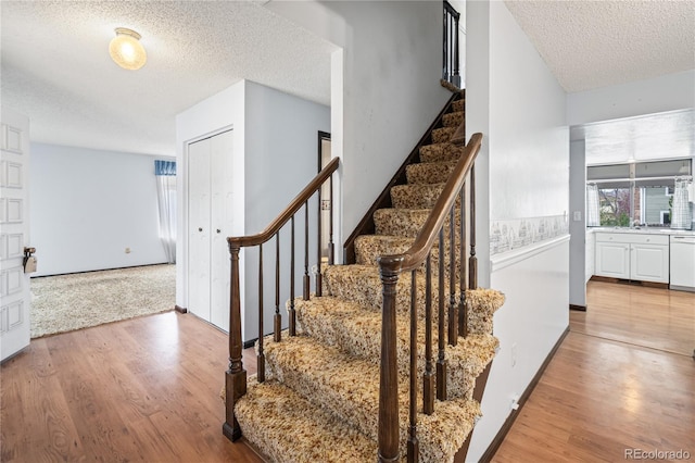 stairway with a textured ceiling, baseboards, and wood finished floors