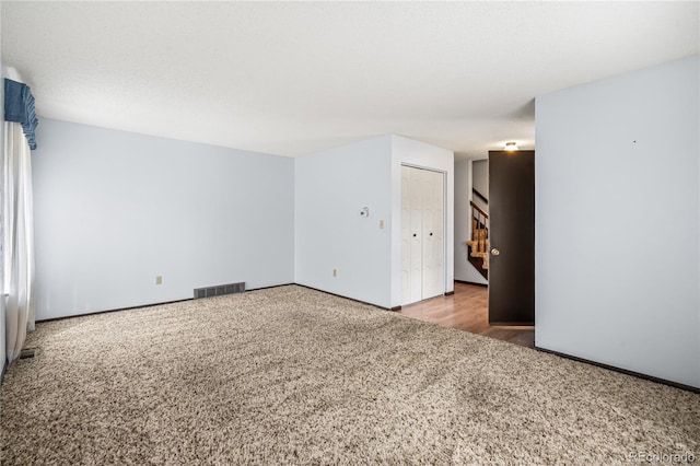 carpeted empty room featuring visible vents and stairway