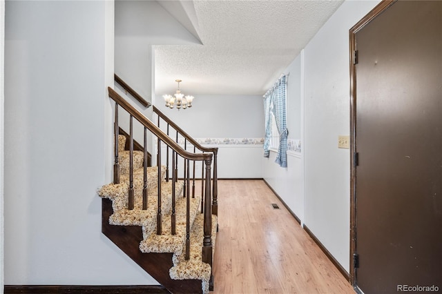 foyer entrance with baseboards, light wood-type flooring, an inviting chandelier, a textured ceiling, and visible vents