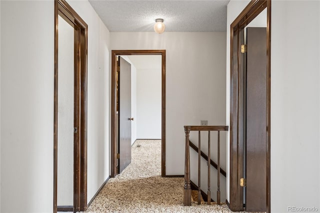 corridor featuring an upstairs landing, a textured ceiling, and carpet