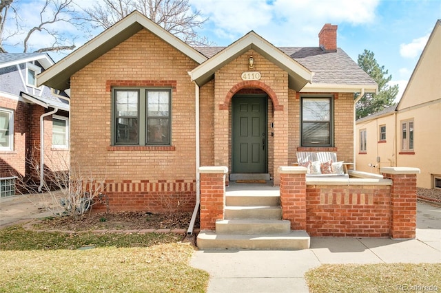 bungalow-style house featuring brick siding, a chimney, and roof with shingles