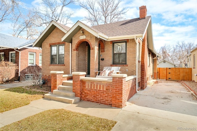 view of front of house with brick siding, a shingled roof, a chimney, and fence