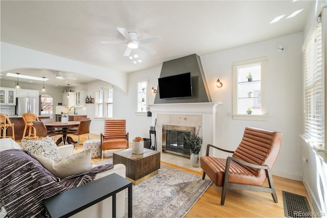 living room featuring visible vents, light wood-style flooring, arched walkways, a fireplace, and ceiling fan