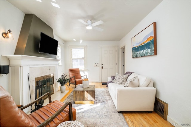 living area with visible vents, a ceiling fan, light wood-style floors, baseboards, and a tile fireplace