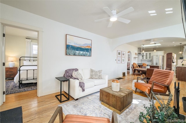 living area with arched walkways, baseboards, light wood-type flooring, and a ceiling fan