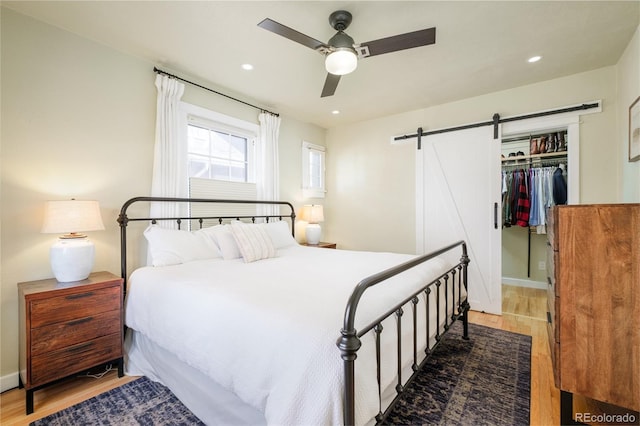 bedroom with light wood-type flooring, recessed lighting, a barn door, a closet, and ceiling fan