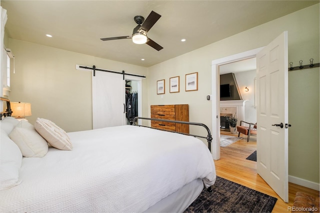 bedroom with a ceiling fan, light wood-style flooring, recessed lighting, a fireplace, and a barn door