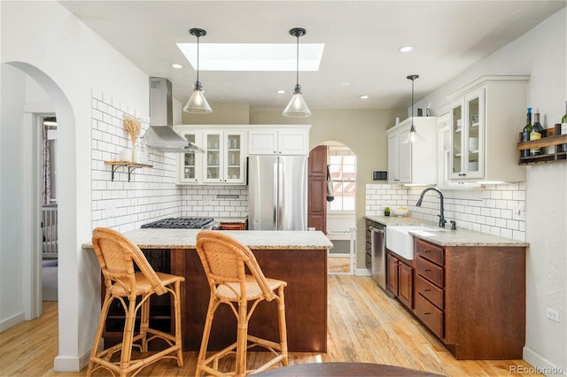 kitchen with appliances with stainless steel finishes, a peninsula, arched walkways, wall chimney exhaust hood, and a sink