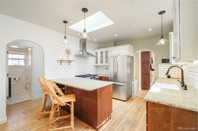 kitchen featuring a sink, light stone countertops, appliances with stainless steel finishes, and wall chimney range hood