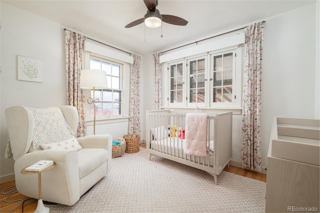 bedroom with a crib, wood finished floors, a ceiling fan, and baseboards