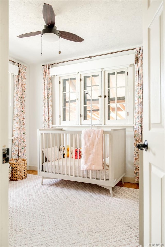 bedroom with ceiling fan, multiple windows, a nursery area, and a textured ceiling