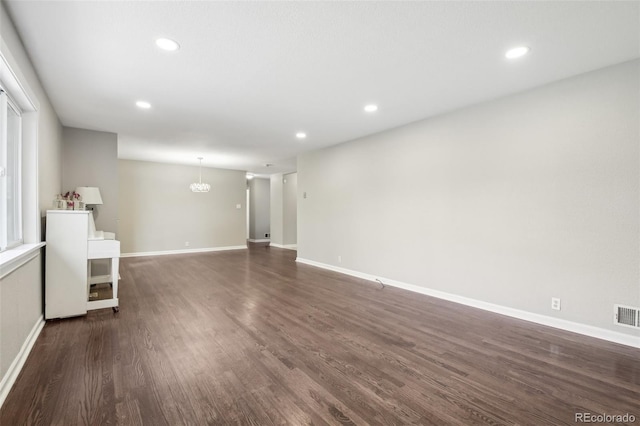 unfurnished living room with dark wood-type flooring, recessed lighting, baseboards, and a chandelier
