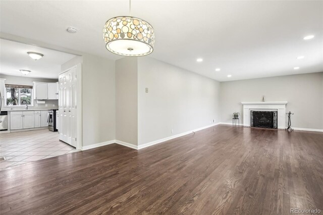 unfurnished living room featuring wood finished floors, recessed lighting, baseboards, a fireplace, and a sink