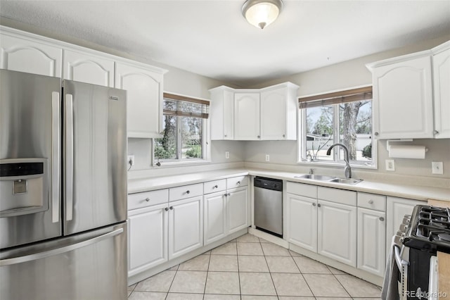 kitchen with appliances with stainless steel finishes, a sink, white cabinetry, and light tile patterned floors