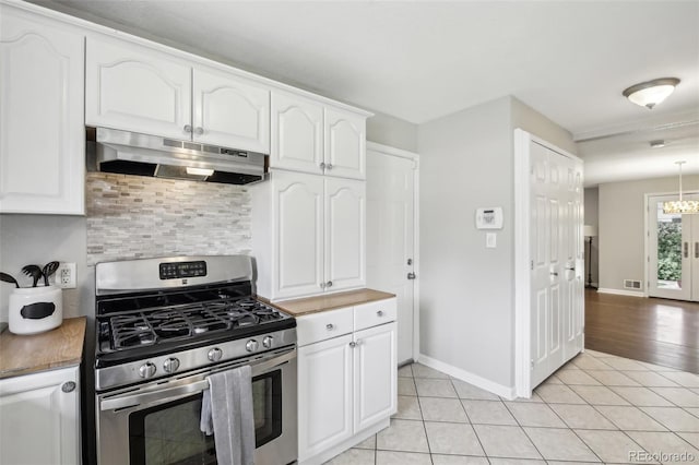 kitchen featuring stainless steel range with gas cooktop, under cabinet range hood, tasteful backsplash, light tile patterned floors, and white cabinetry