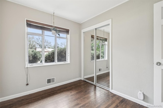 unfurnished bedroom with a chandelier, multiple windows, dark wood-type flooring, and a closet