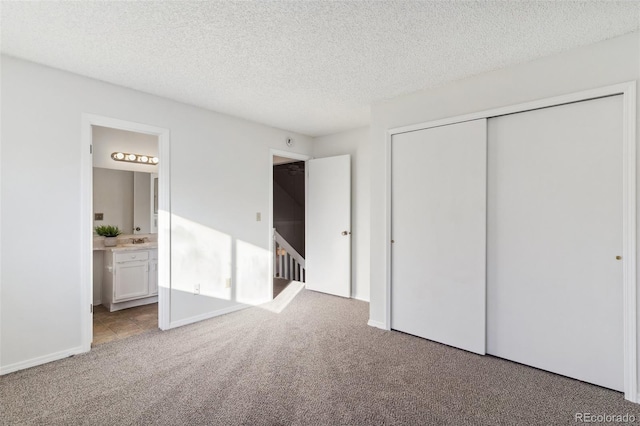 unfurnished bedroom with a textured ceiling, a closet, connected bathroom, and light colored carpet