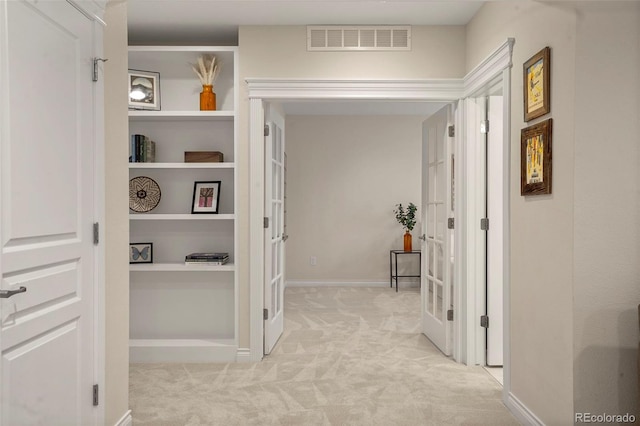 corridor with light colored carpet, baseboards, visible vents, and built in shelves