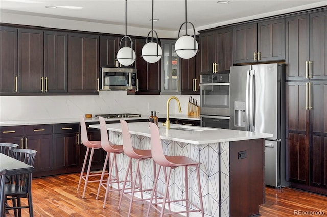 kitchen featuring a sink, a kitchen bar, wood finished floors, a center island with sink, and stainless steel appliances
