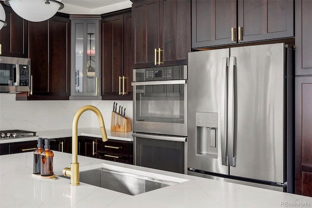 kitchen with a sink, appliances with stainless steel finishes, dark brown cabinetry, and glass insert cabinets