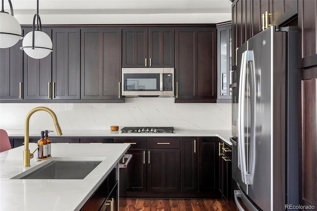 kitchen with a sink, stainless steel appliances, dark wood-type flooring, light stone countertops, and hanging light fixtures