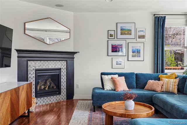 living room featuring baseboards, a tiled fireplace, and dark wood-style floors
