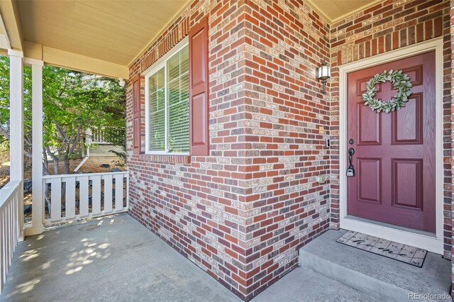 entrance to property with a porch and brick siding