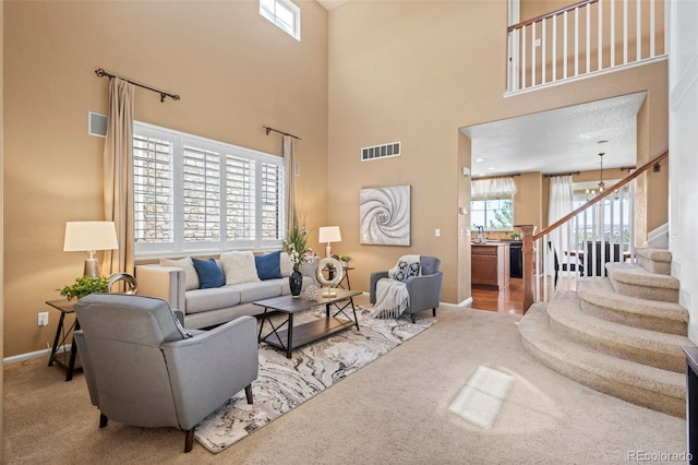 carpeted living room with visible vents, a high ceiling, stairs, and baseboards