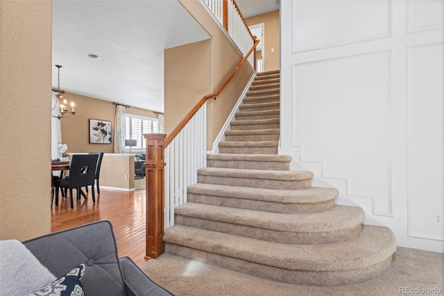 stairway with baseboards, an inviting chandelier, and wood finished floors