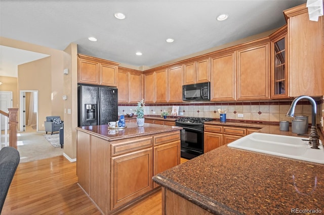 kitchen featuring a sink, a center island, decorative backsplash, light wood-type flooring, and black appliances
