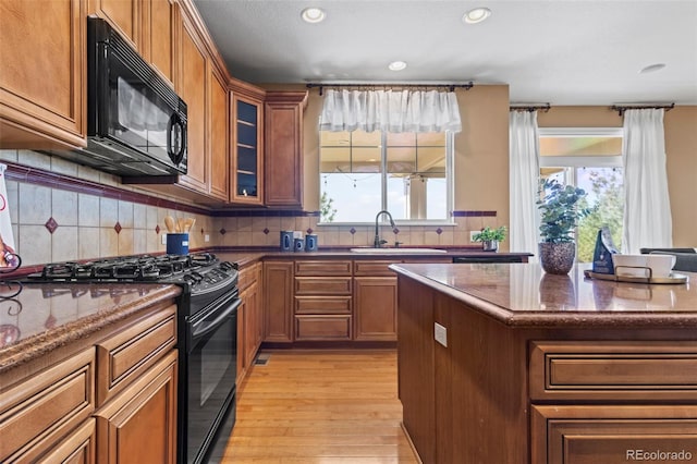 kitchen featuring light wood-type flooring, a sink, black appliances, and a healthy amount of sunlight