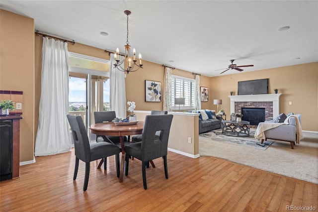 dining room with baseboards, light wood-style flooring, ceiling fan with notable chandelier, and a fireplace