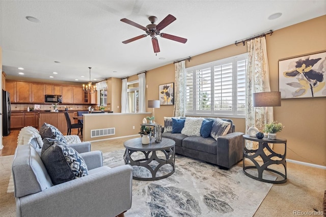 living area with baseboards, ceiling fan with notable chandelier, visible vents, and light colored carpet