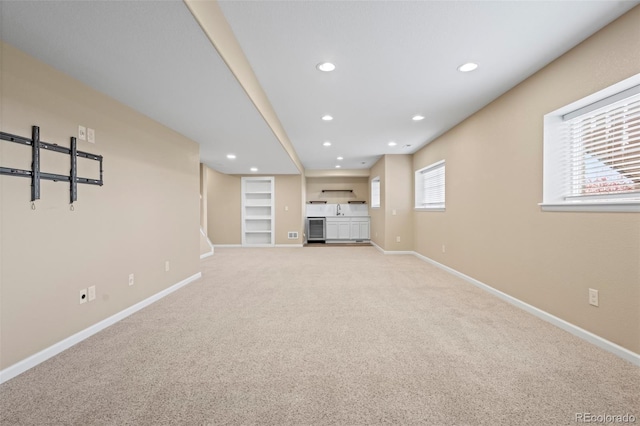 unfurnished living room featuring baseboards, recessed lighting, built in shelves, and light colored carpet