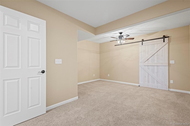 spare room featuring baseboards, ceiling fan, carpet, and a barn door