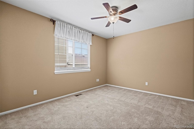 empty room with carpet flooring, a ceiling fan, baseboards, and visible vents