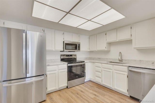 kitchen featuring white cabinets, light wood-style flooring, appliances with stainless steel finishes, light stone countertops, and a sink