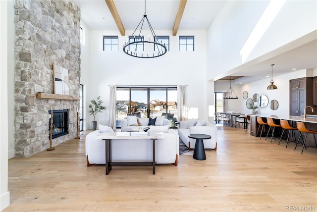 living room with a towering ceiling, beamed ceiling, a stone fireplace, and light hardwood / wood-style floors