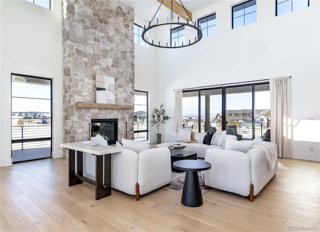 living room with light wood-type flooring, an inviting chandelier, a towering ceiling, and a fireplace