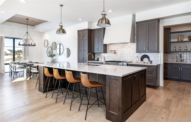 kitchen featuring a spacious island, custom exhaust hood, light hardwood / wood-style floors, a breakfast bar, and dark brown cabinets