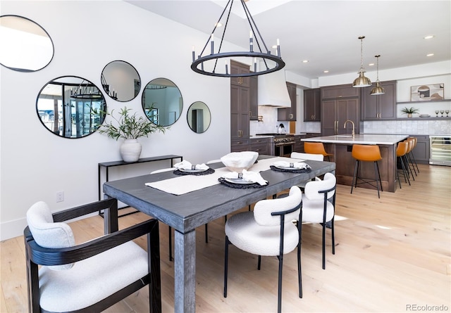 dining space with sink, wine cooler, a chandelier, and light wood-type flooring