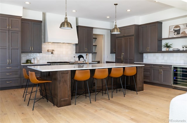 kitchen featuring wine cooler, custom exhaust hood, a breakfast bar, light hardwood / wood-style flooring, and a kitchen island with sink